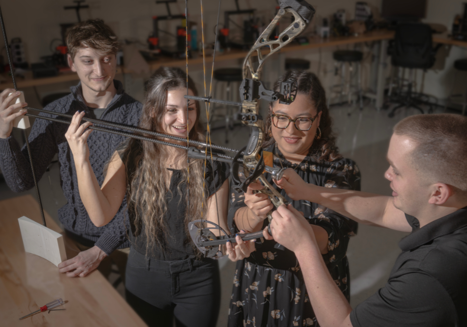 four students work with an archery assist device