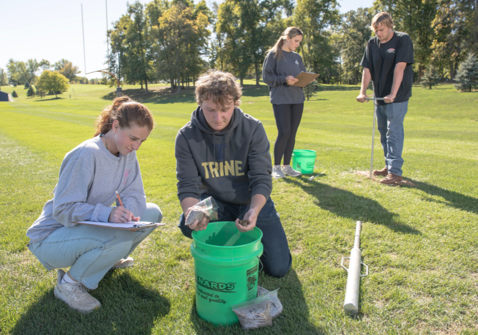two students test soil from the ground while two other students test soil in a bucket