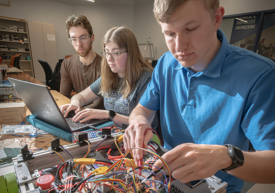 three students working with wires and a laptop