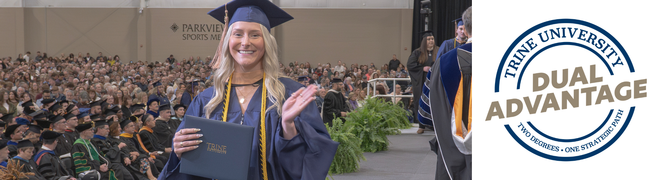 trine student in graduation regalia and master's hood smiling as she crosses the commencement stage