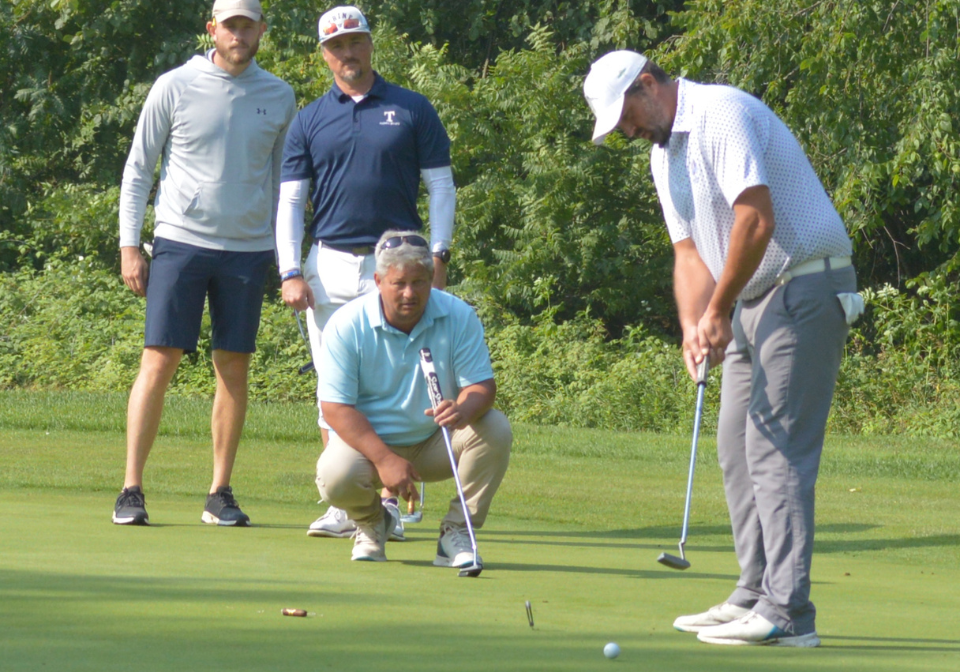 group of men intently watch as golf ball nears the hole