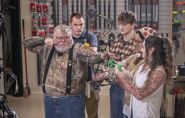 Veteran Chester Evitt holding bow with Trine University students