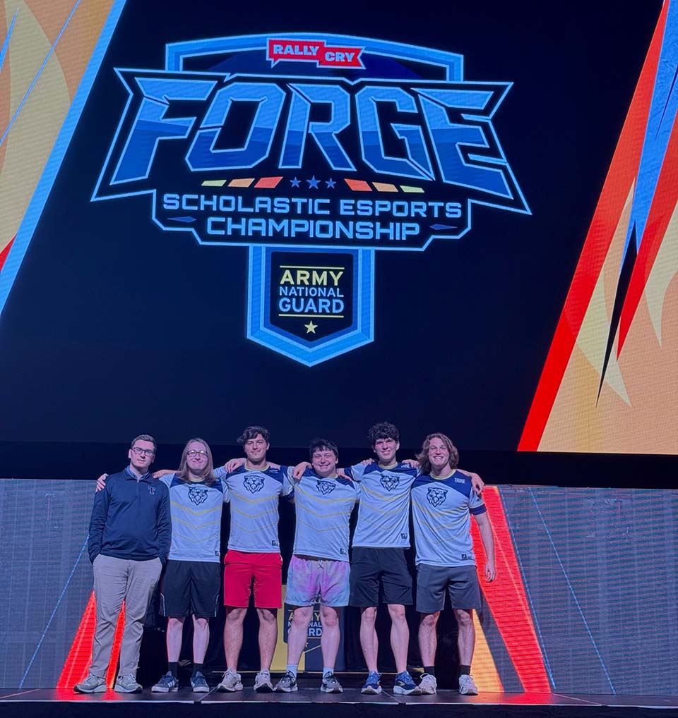 Esports director and five students on stage in front of logo.