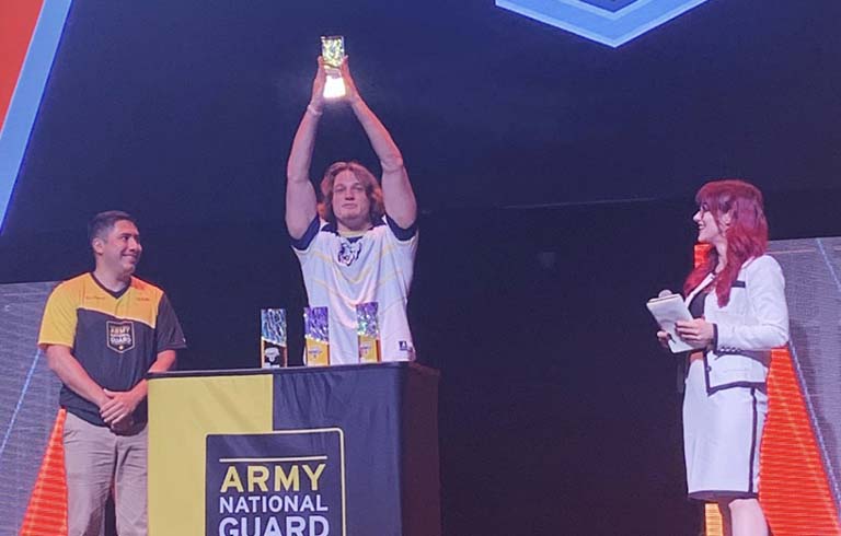 Student holding trophy up in the middle of two esports officials.