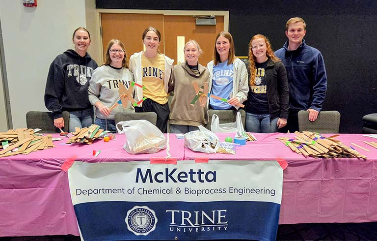 Students standing behind table with pink tablecloth and McKetta Department of Chemical & Bioprocess Engineering banner