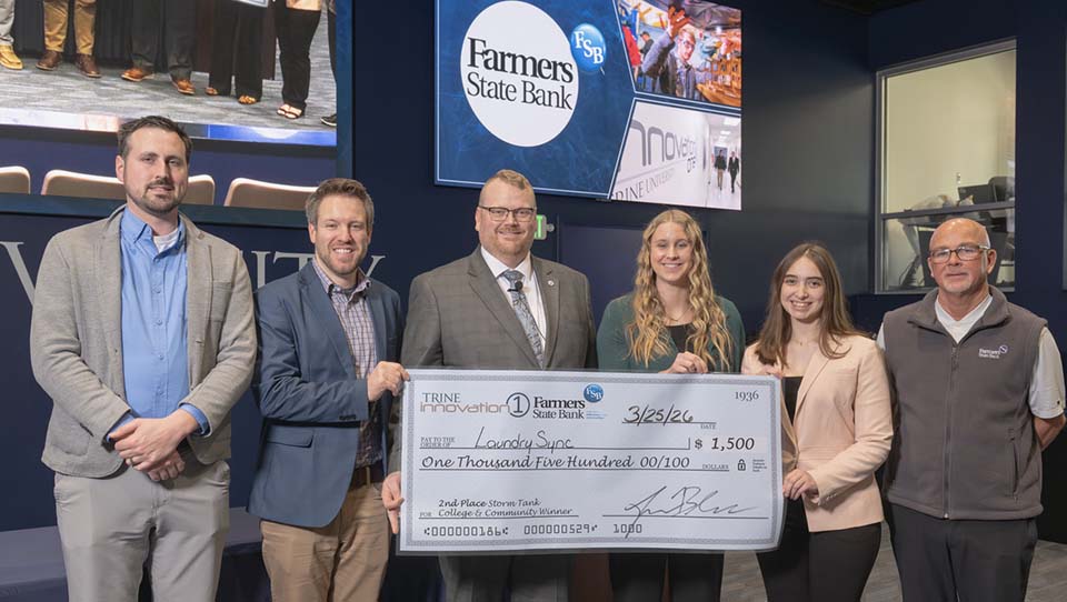 Three bank executives and one college administrator presenting large check to two students.