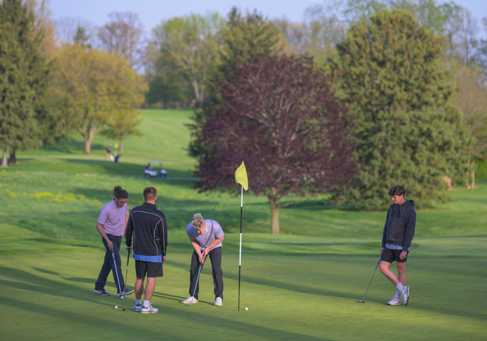 four students watching a ball approach a hole on zollner golf course
